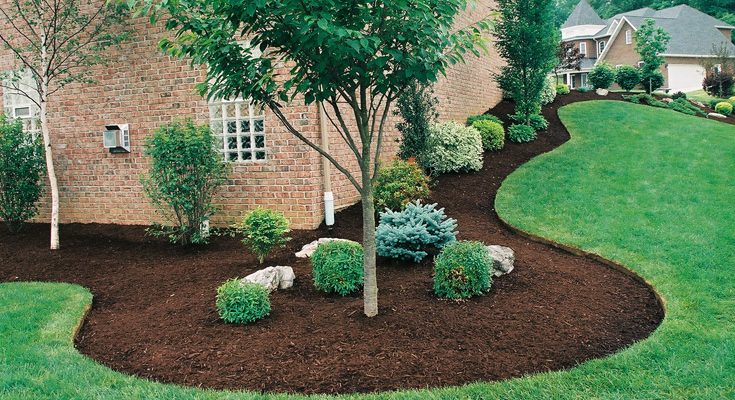 Landscaping & Mulching Services Lush green lawn with landscaped flower beds with mulch and decorative rocks.